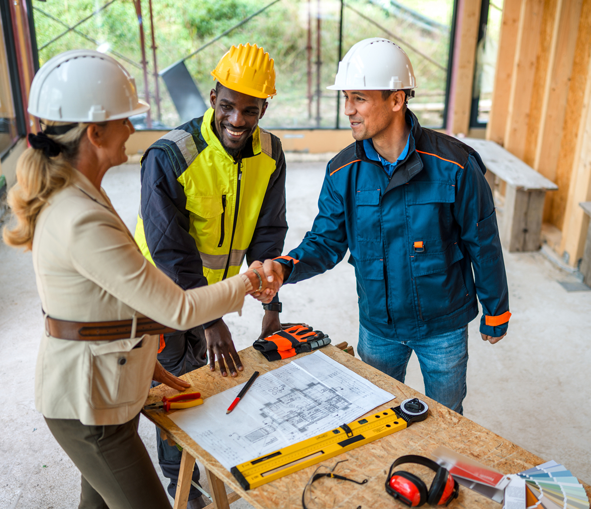 Construction workers shaking hands over plans.