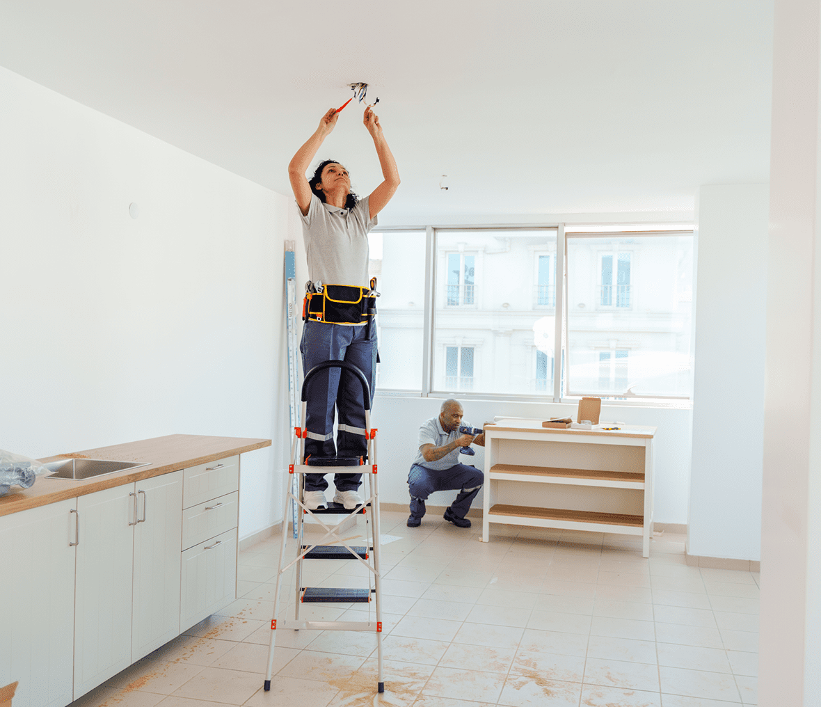 Person fixing ceiling light on ladder indoors.
