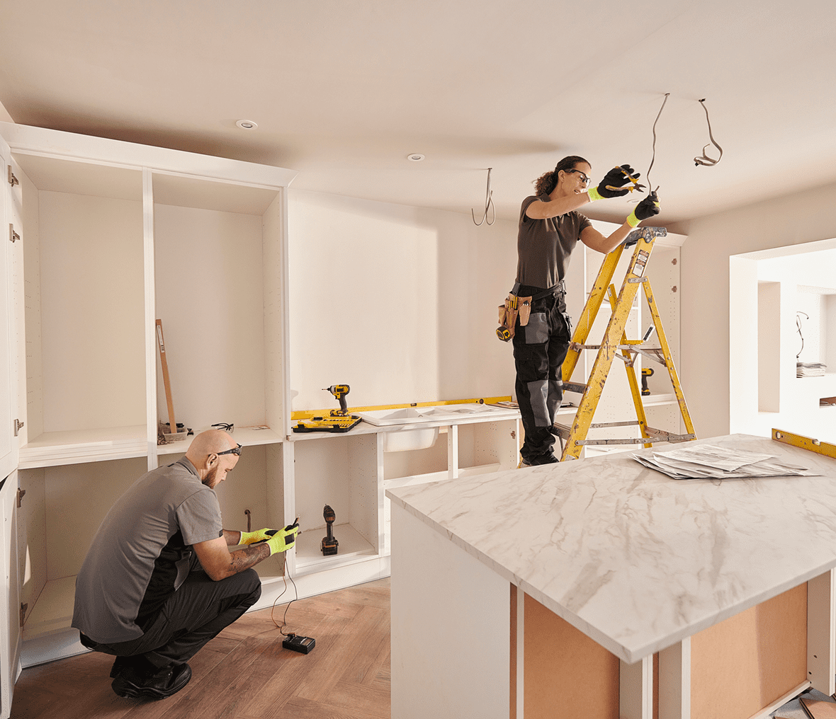 Workers installing cabinets and lighting in kitchen.