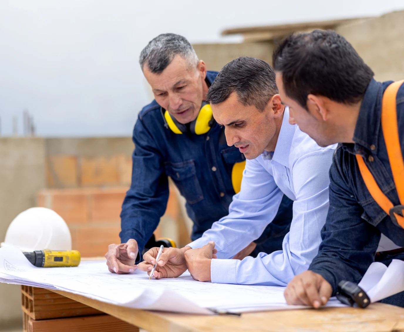 Three men discussing construction plans at site.